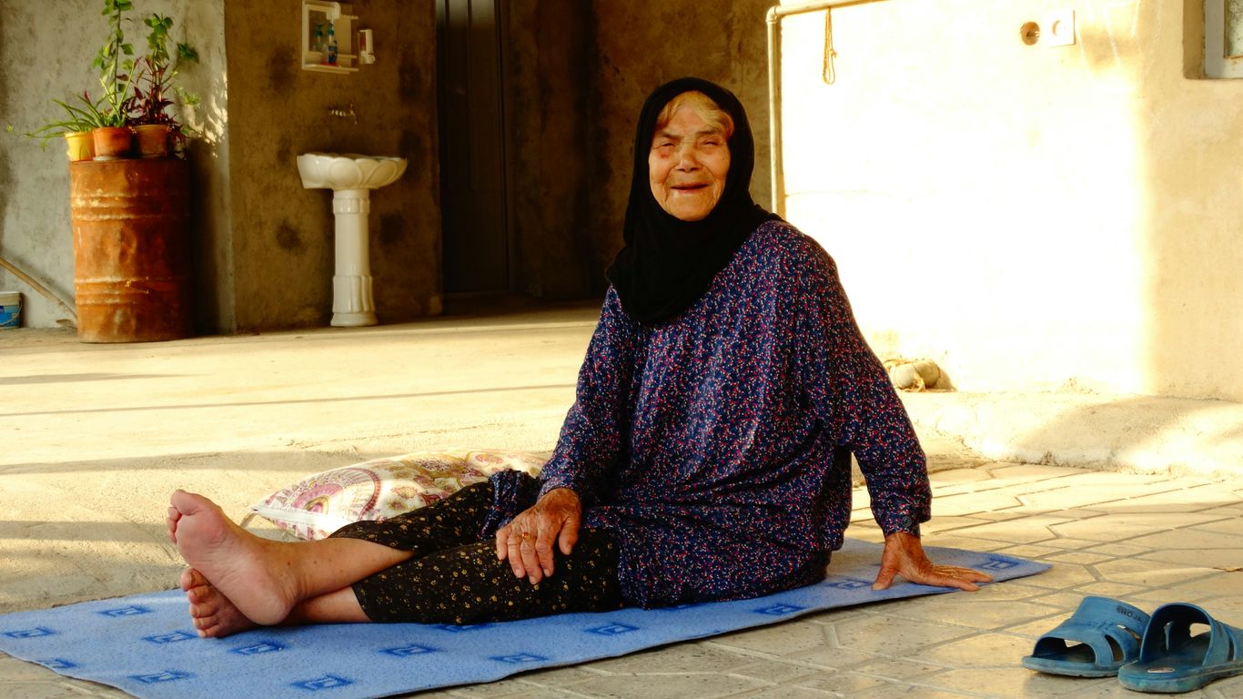 An elderly woman smiles while sitting outside.