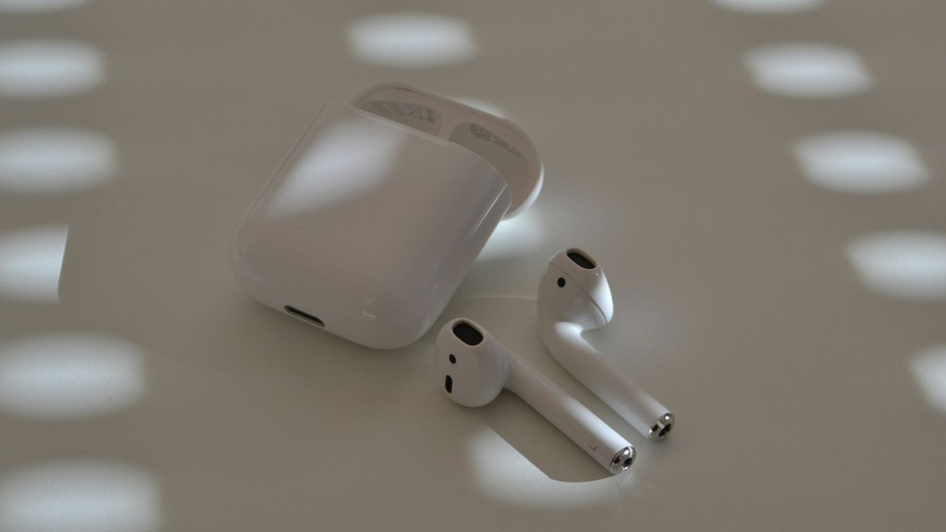 Airpods and their case sit on a white surface.