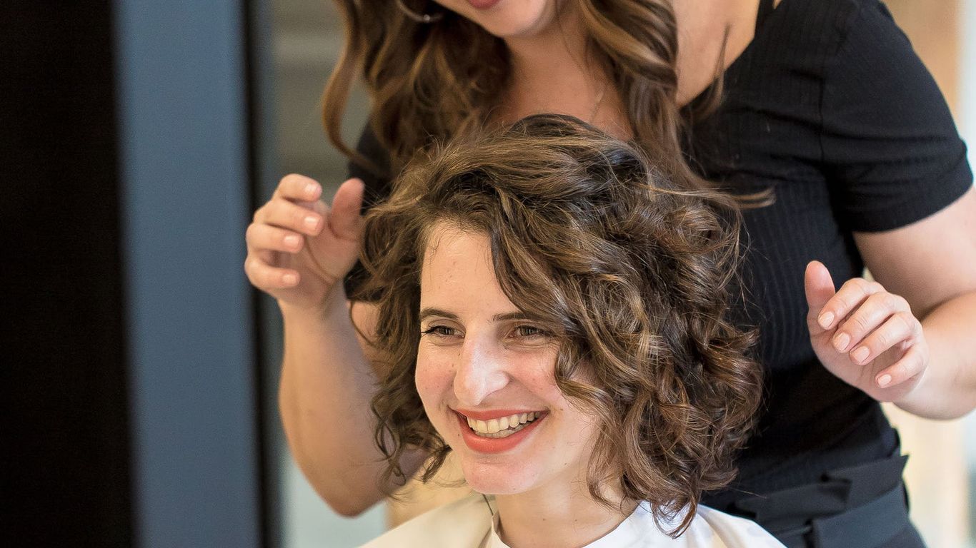 Hairstylist showcasing finished curly hairstyle on happy female client.