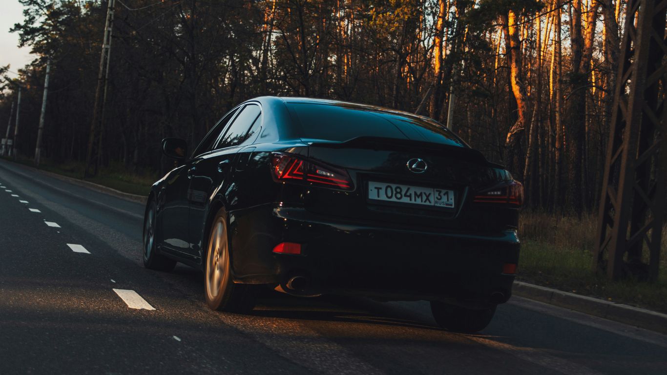 Black sedan driving on a road at sunset.