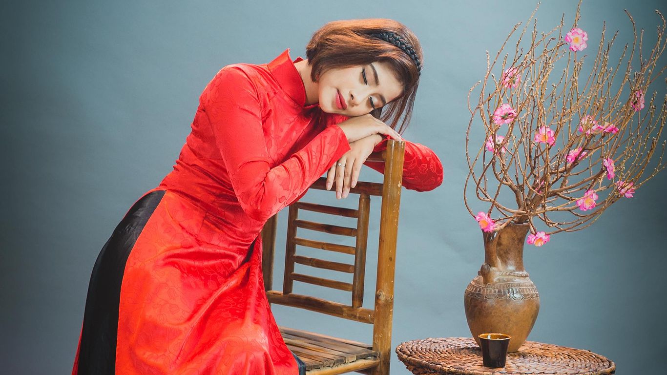 Person in red dress resting on chair beside flower vase.