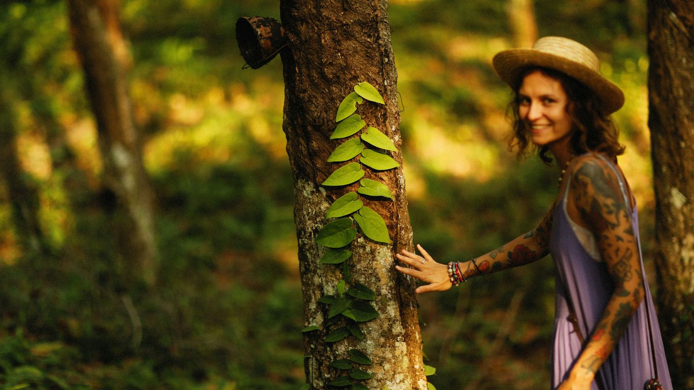 a woman in a purple dress and hat standing next to a tree
