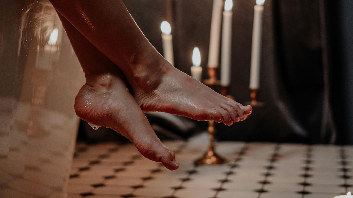 Person relaxing in bathtub, candles lit, water on floor.