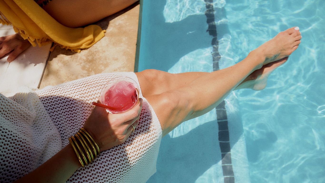Person relaxing by the pool with a drink and wearing jewelry.