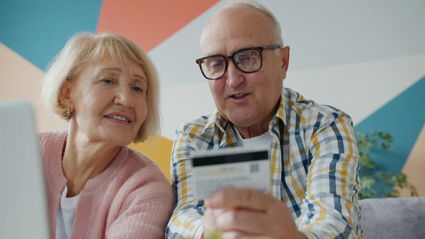 Elderly couple looking at credit card and laptop.