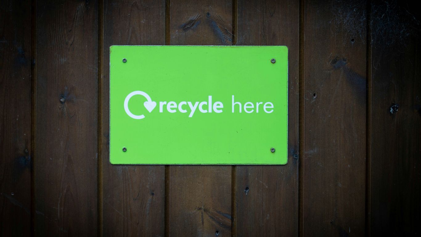 a green recycle here sign on a wooden wall