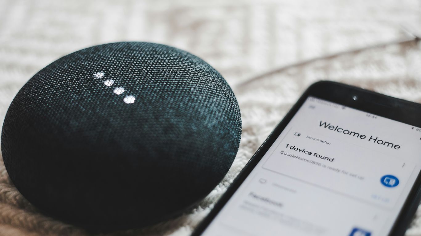 turned-on charcoal Google Home Mini and smartphone