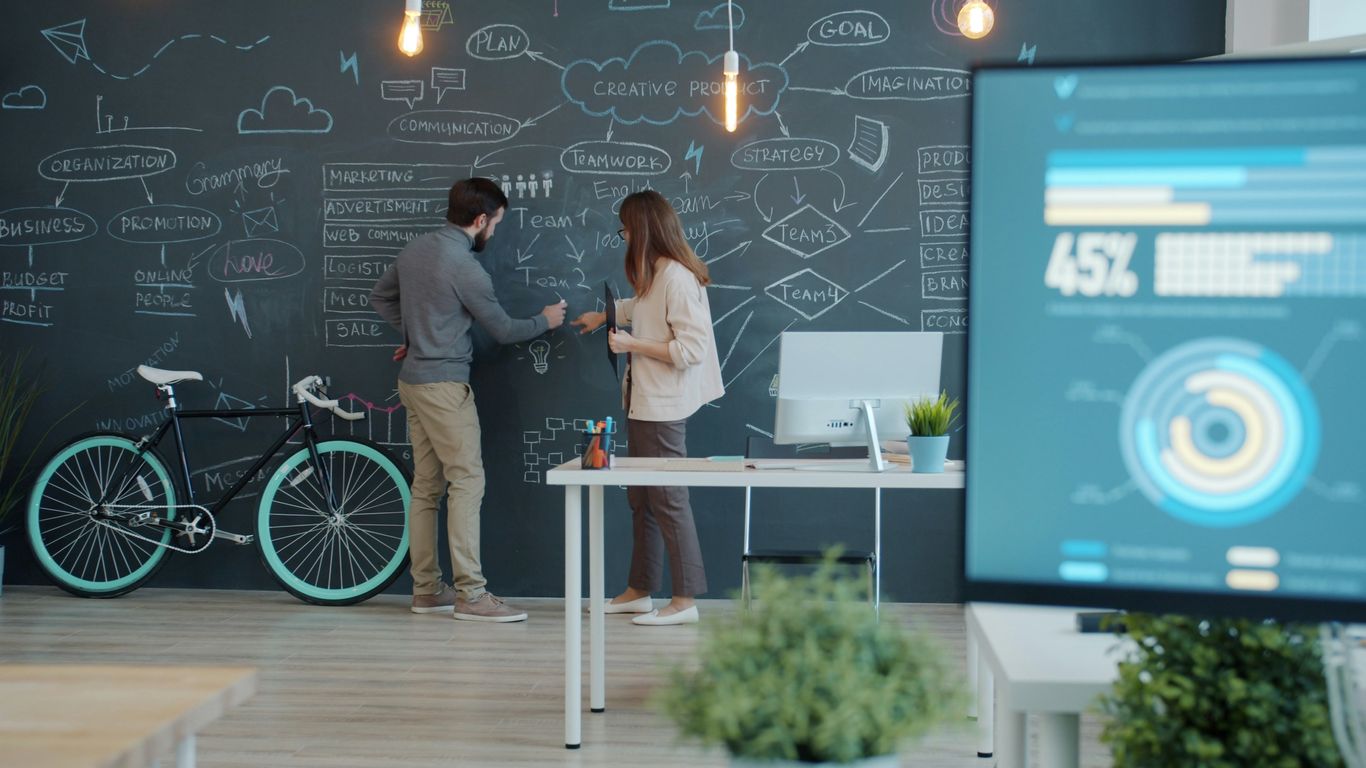 Two people collaborating on a chalkboard with a bicycle.