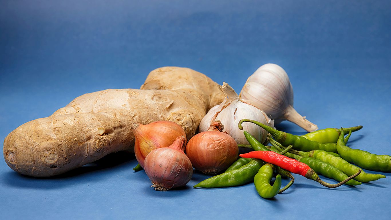 Ginger, garlic, onions, and chili peppers on blue.