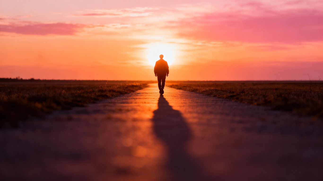 Person walking towards a bright horizon at sunset.