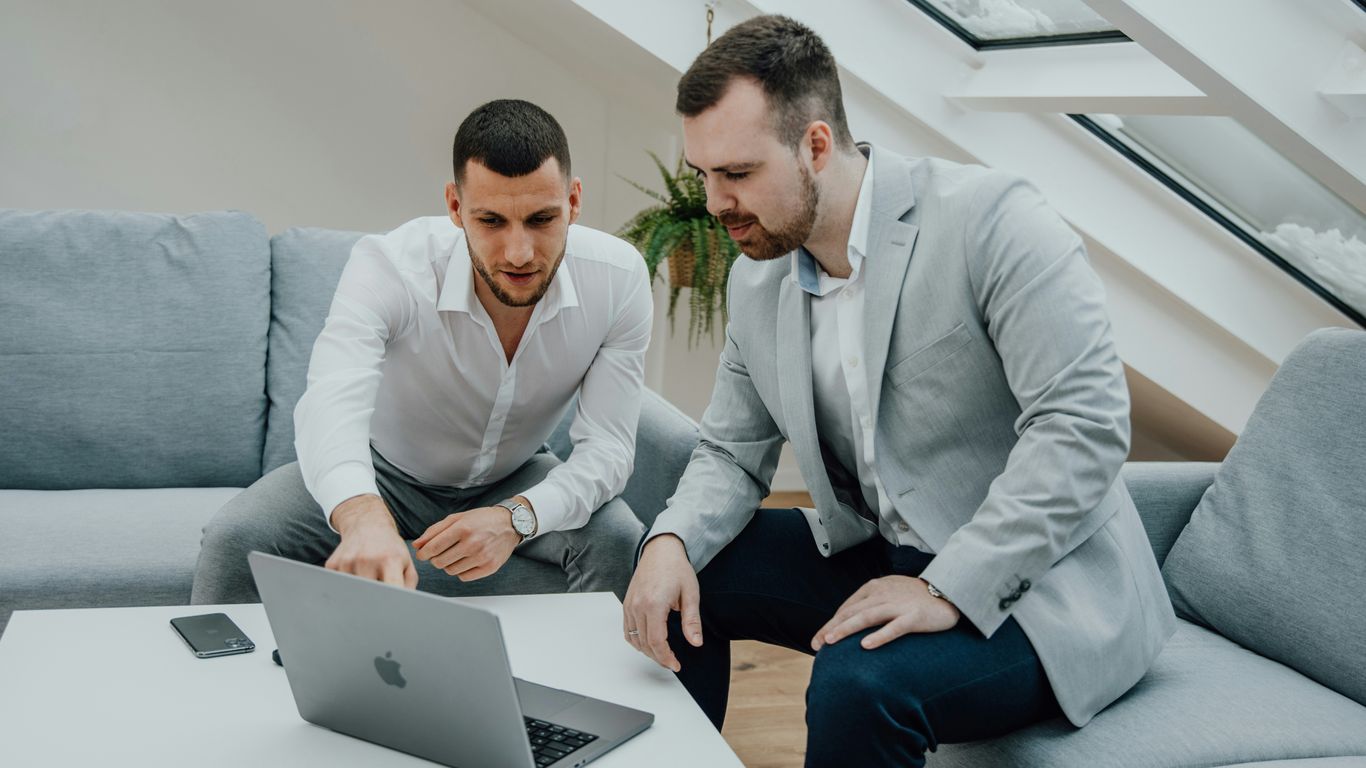 two men looking at a laptop on a table