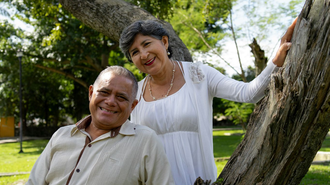 Smiling couple poses near a tree outdoors.