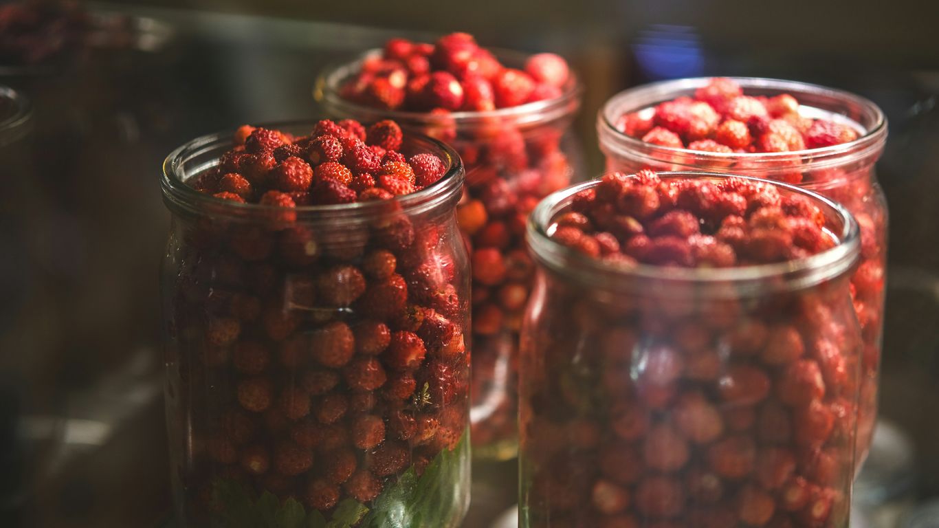 Three jars filled with red berries sitting on top of a table