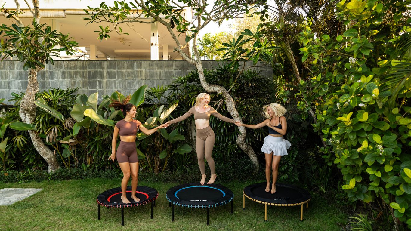 Three people jumping on trampolines outdoors, surrounded by greenery.