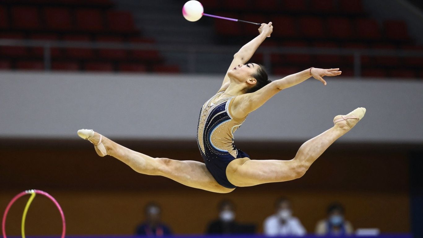 Gimnastă executând un salt acrobatic cu panglică.