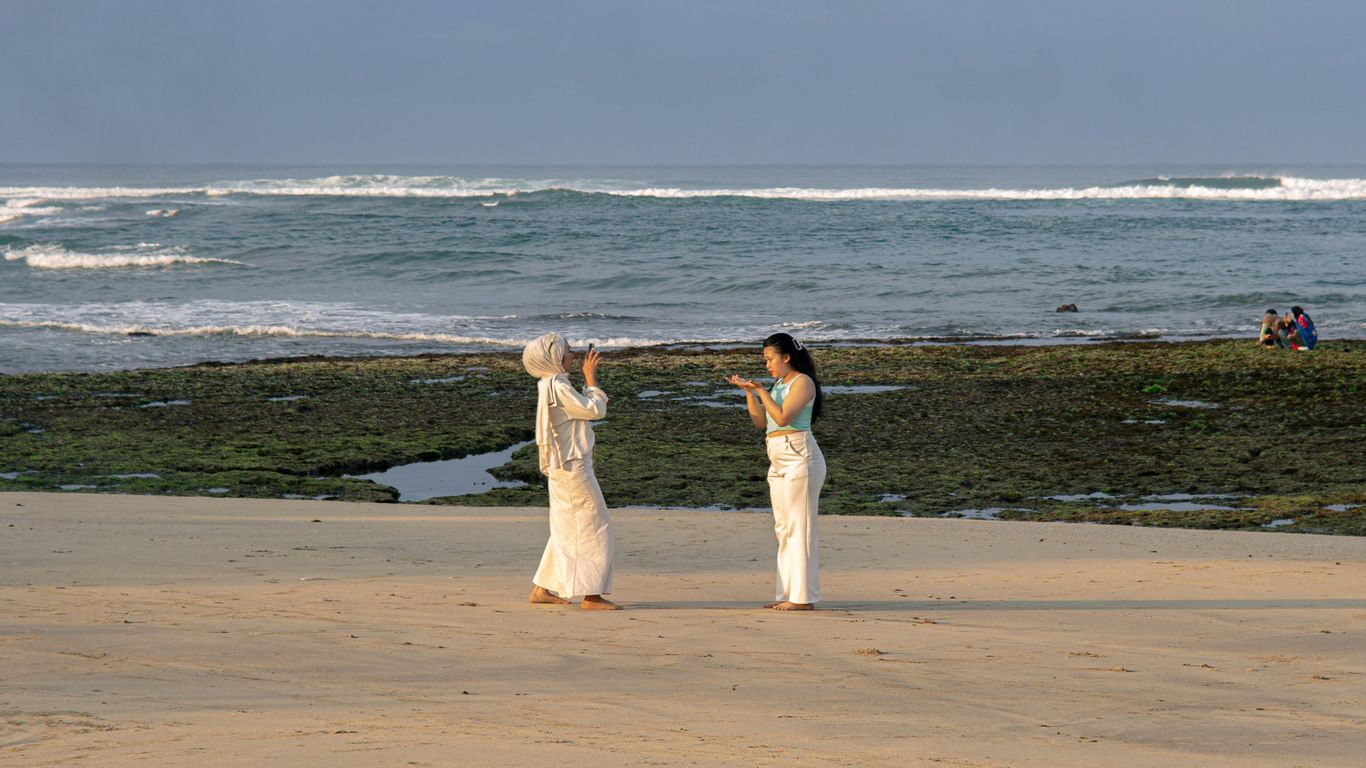 Two women in white on a sandy beach near ocean
