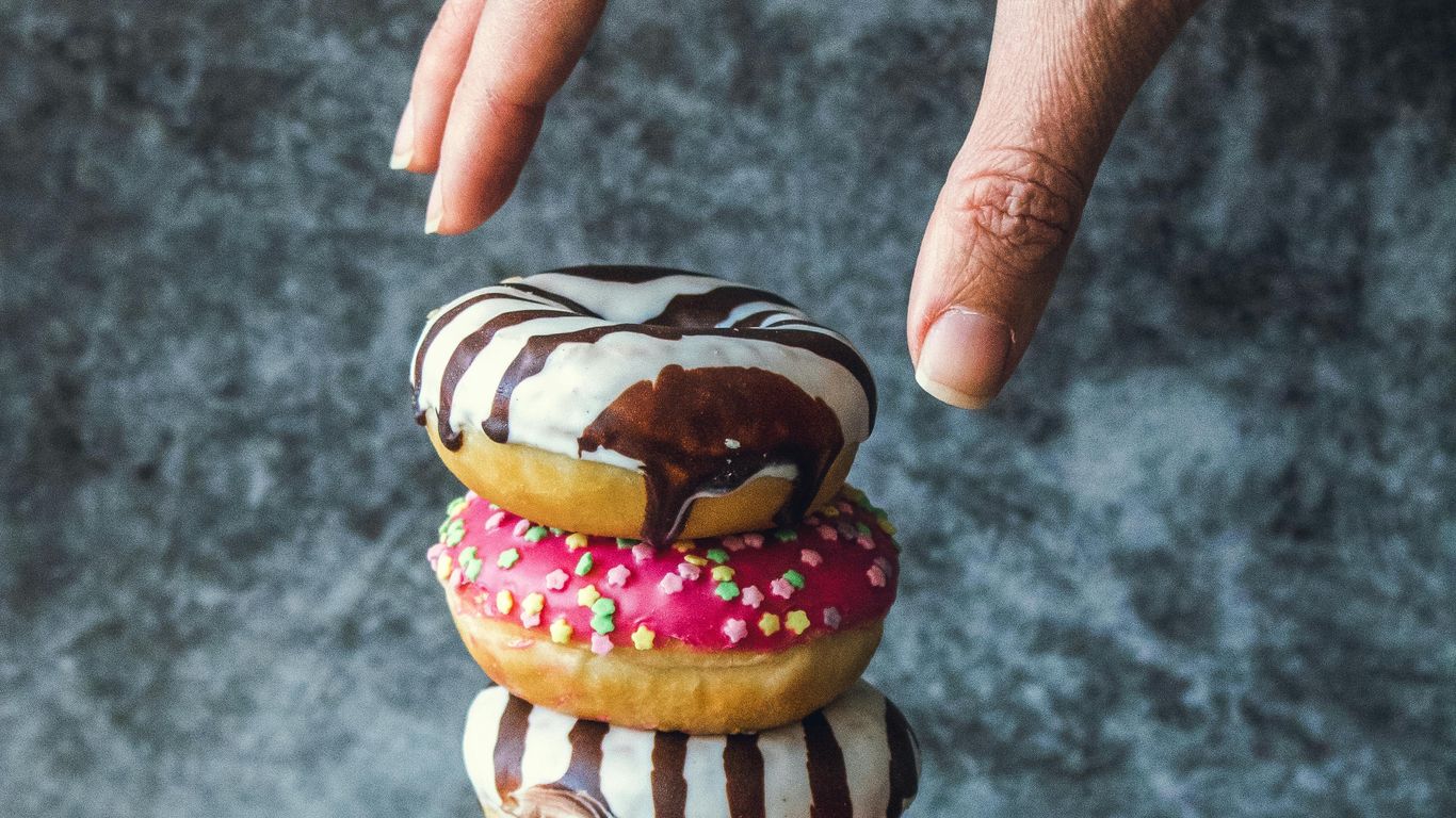 Hand reaching for stacked donuts with colorful icing and sprinkles.