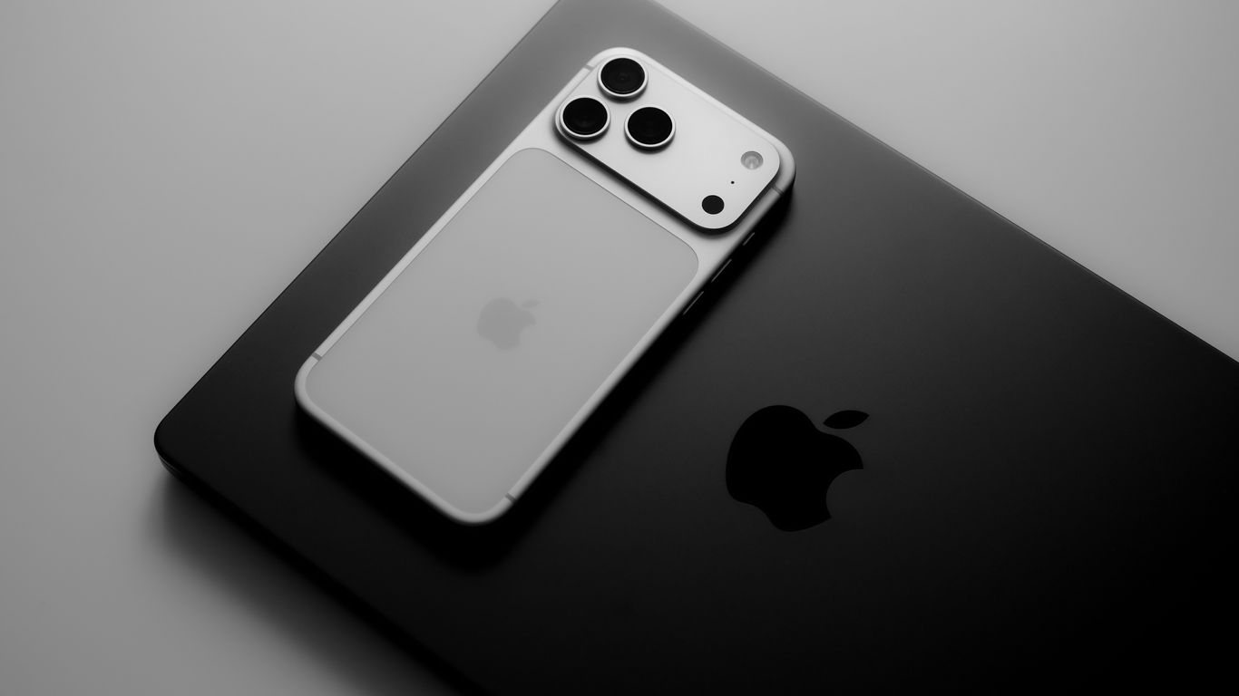 Smartphone resting on laptop with apple logos.