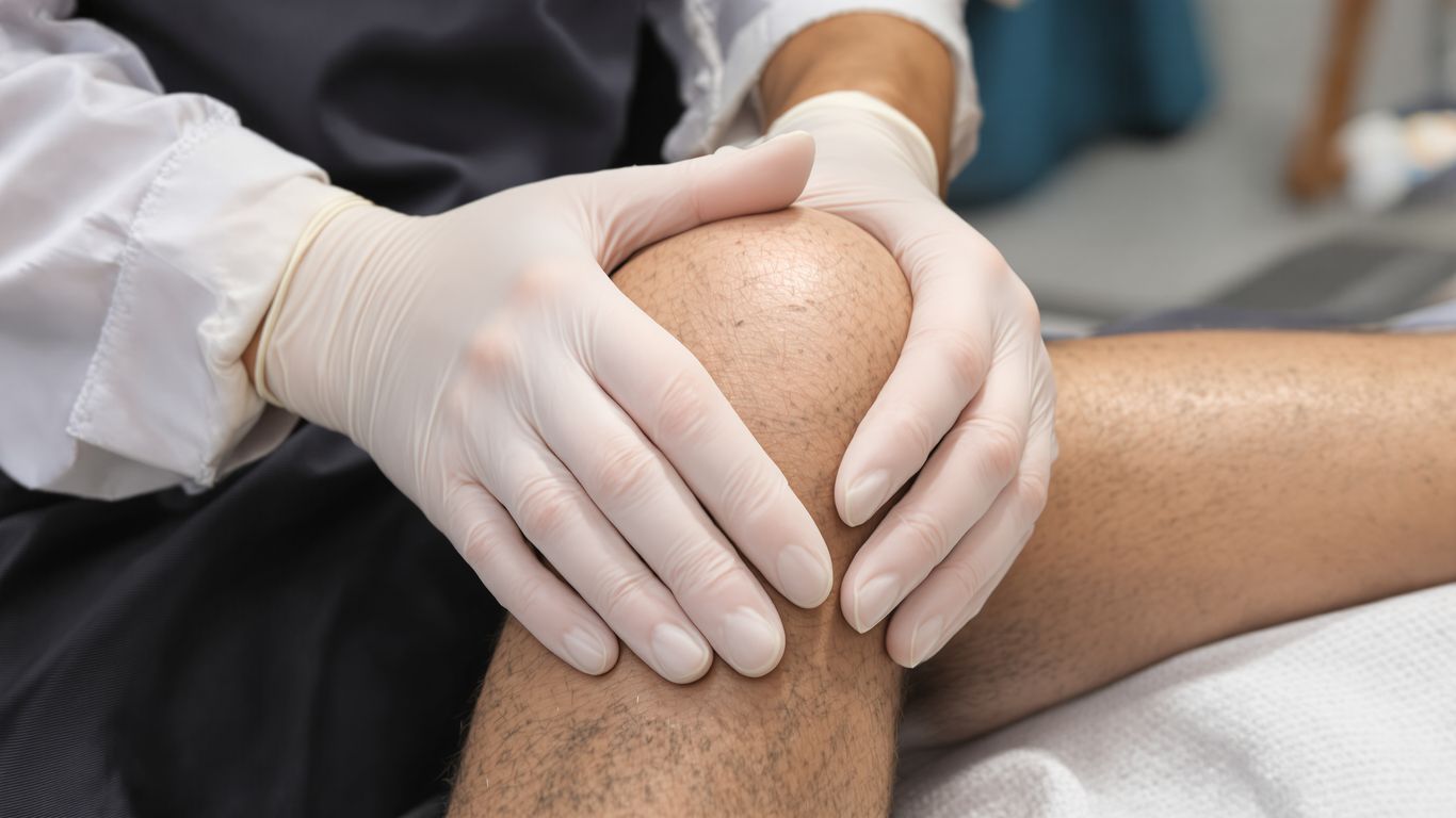Manos de cirujano ortopédico examinando rodilla de paciente.