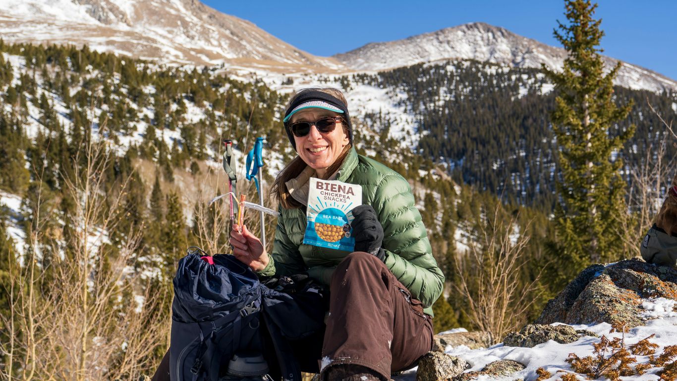 man in green jacket holding green plastic cup sitting on rock during daytime
