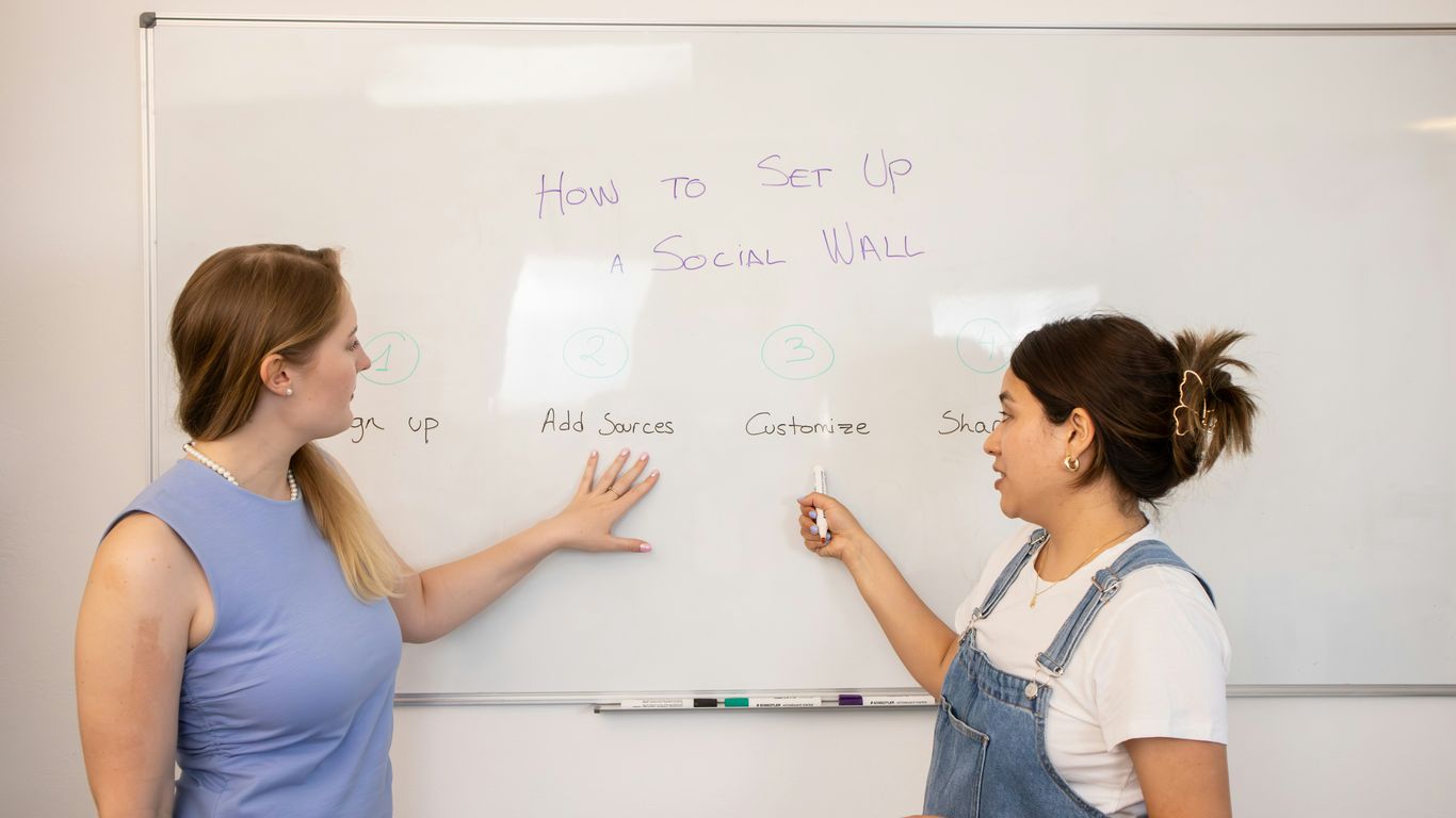 two women standing in front of a whiteboard with writing on it