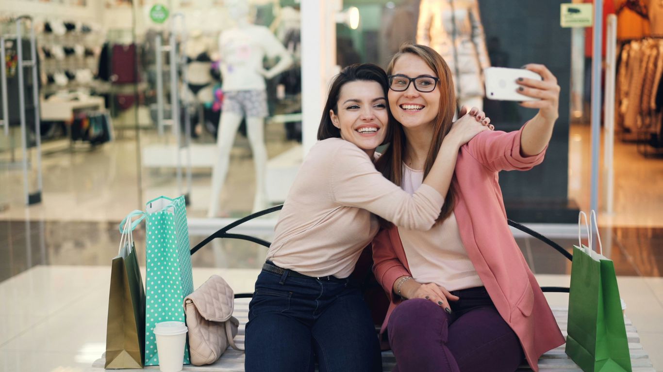 Two smiling women taking a selfie on a bench.