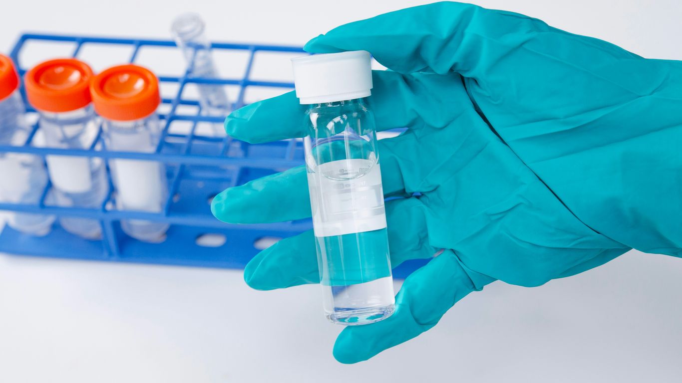 Gloved hand holds vial with clear liquid.