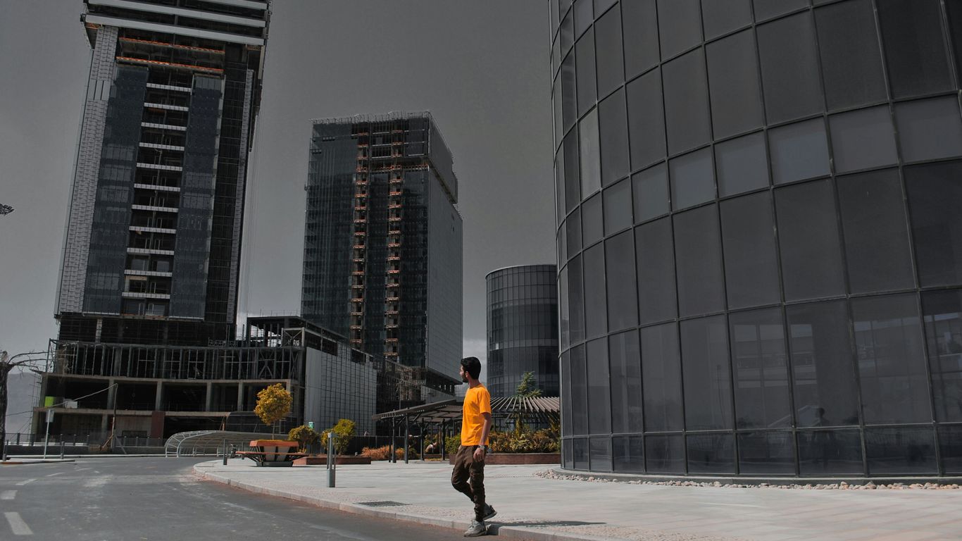 man in yellow jacket and black pants walking on sidewalk near high rise building during daytime