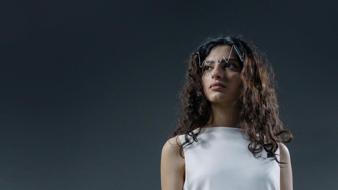 Person with wavy hair wearing white, zigzag accessory on forehead.