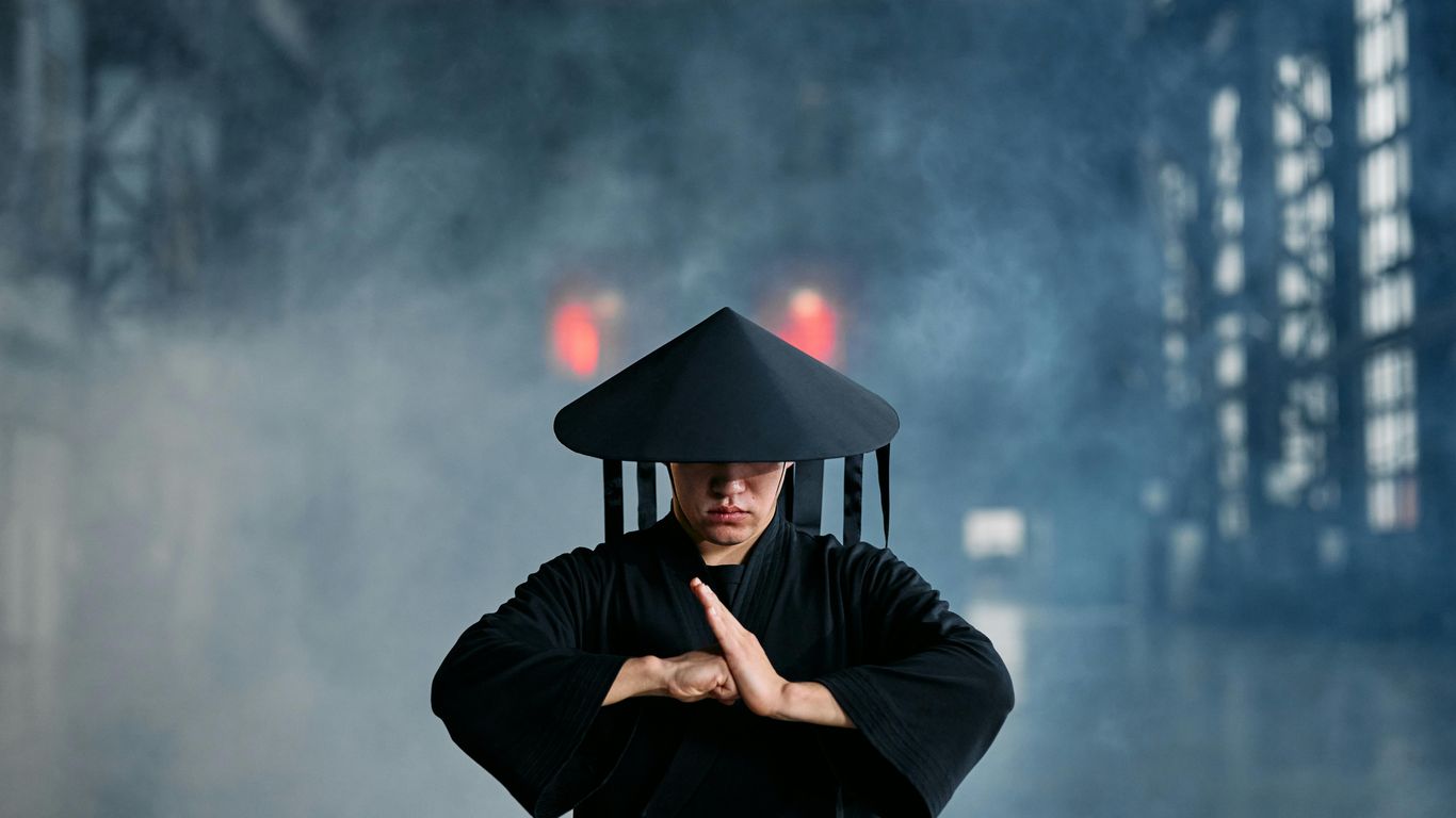 Person in black robe and hat, misty industrial background, meditating.
