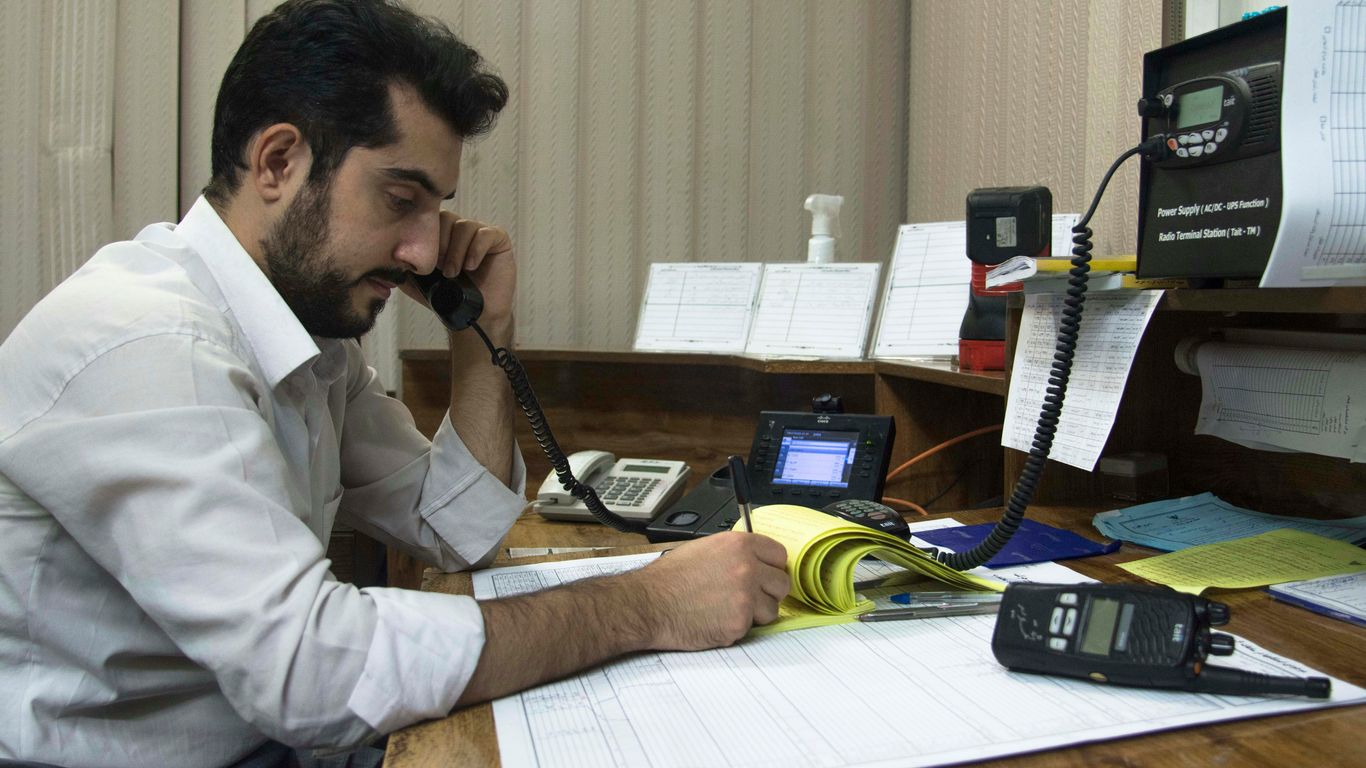 a man sitting at a desk talking on a phone while taking notes on a notepad