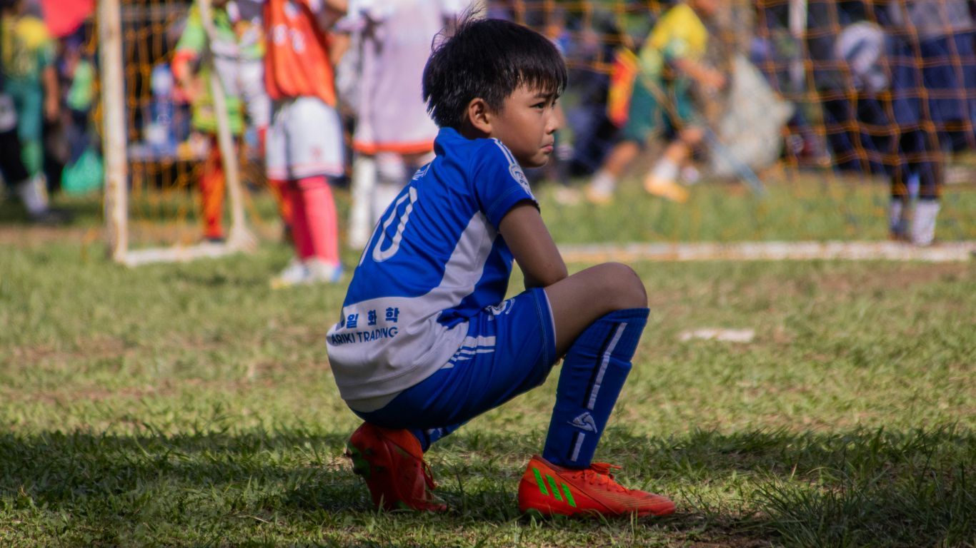 a young boy sitting on the ground during a soccer game