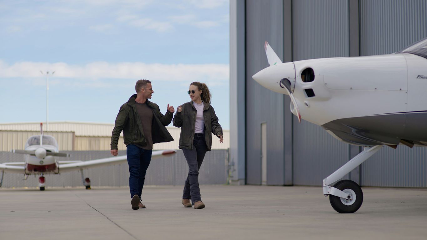 Two people walk by parked airplanes on tarmac.