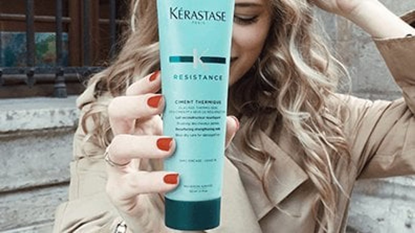 Person holding a Kerastase hair product with a subtle smile.