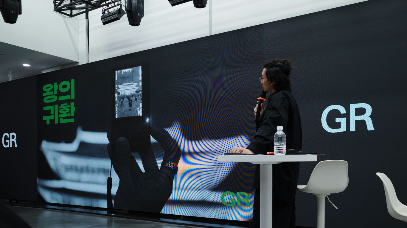 A person speaks at a presentation with a large screen.