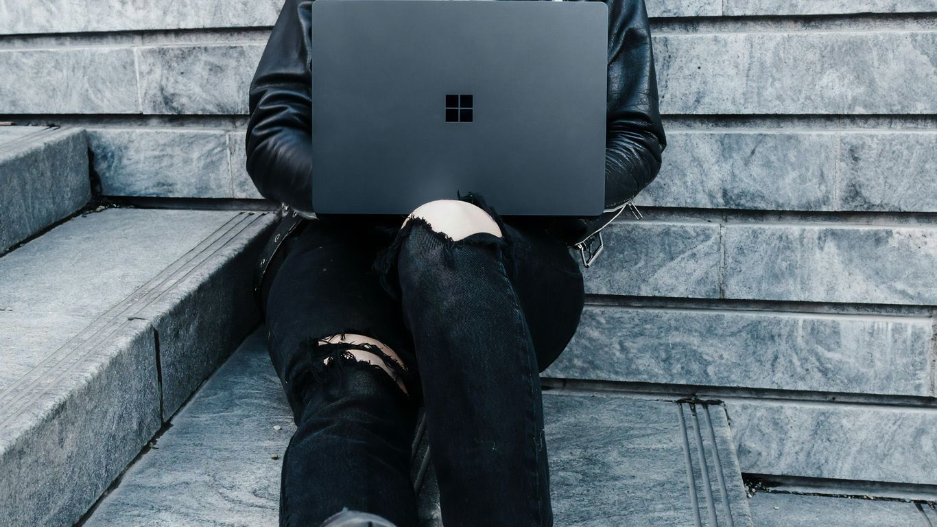 woman in black jacket and black pants sitting on concrete stairs usingMicrosoft Surface Laptop