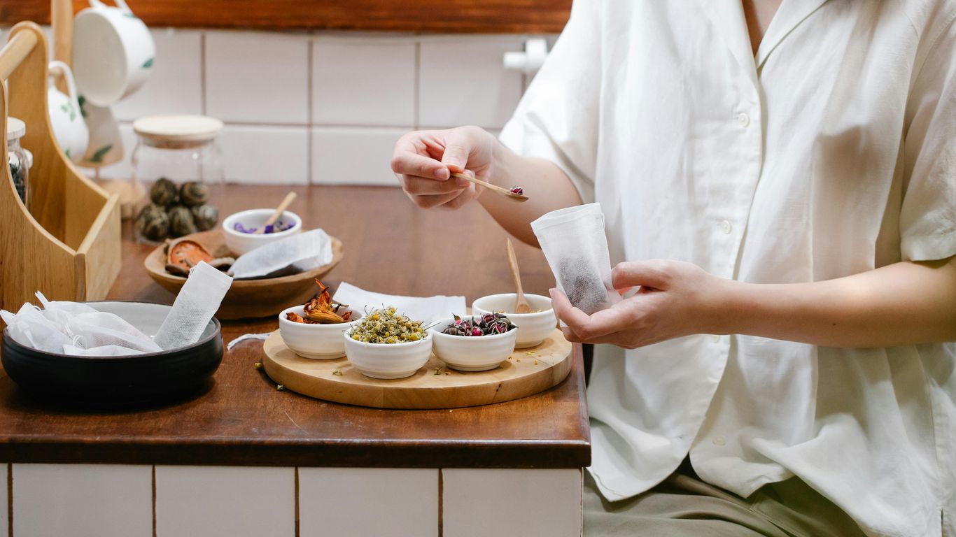 Person preparing tea with various dried herbs and flowers.