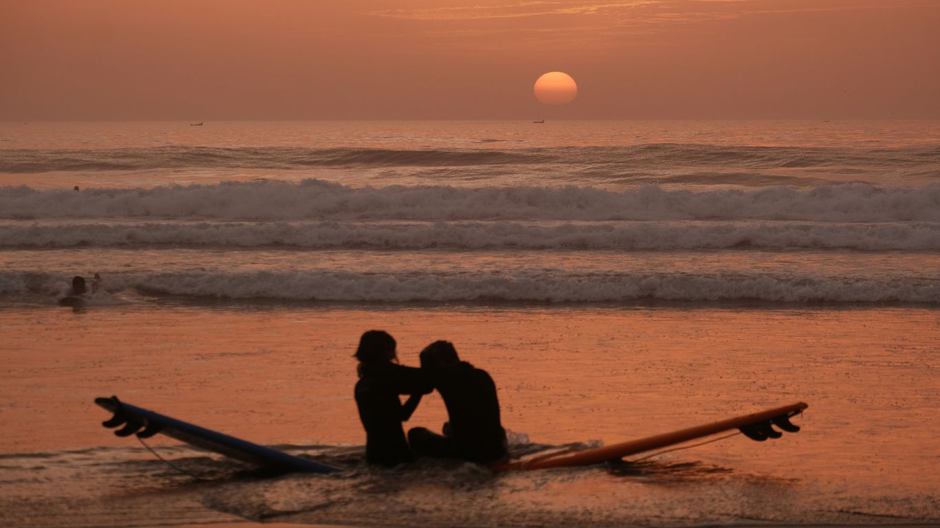 Couple sitting on surfboards at sunset