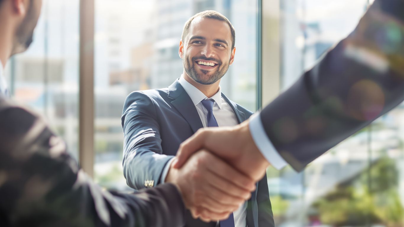 Professional handshake with blurred city background.