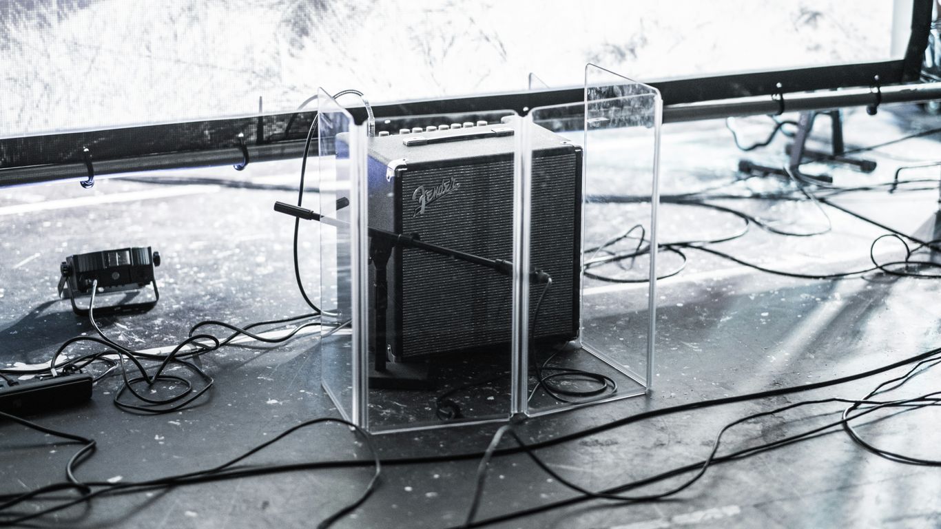 square gray and black Fender guitar amplifier enclosed by clear glass panel on top of stage beside stage lighting