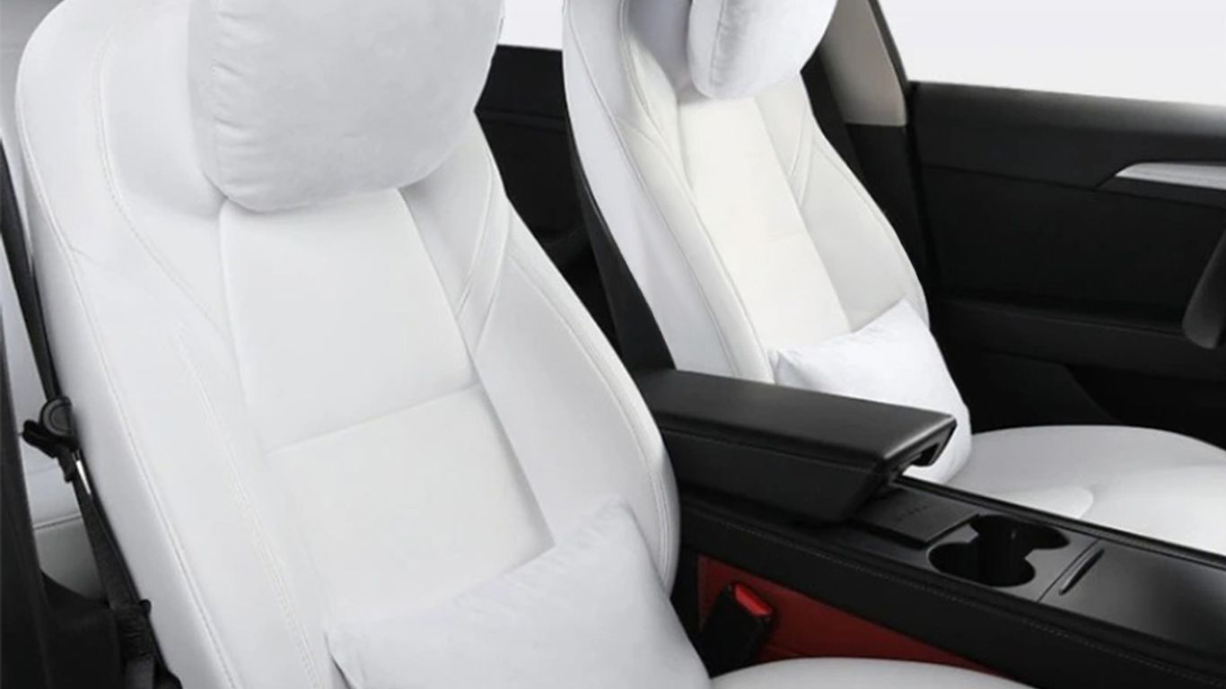 Two white car seats with neck pillows and armrest.