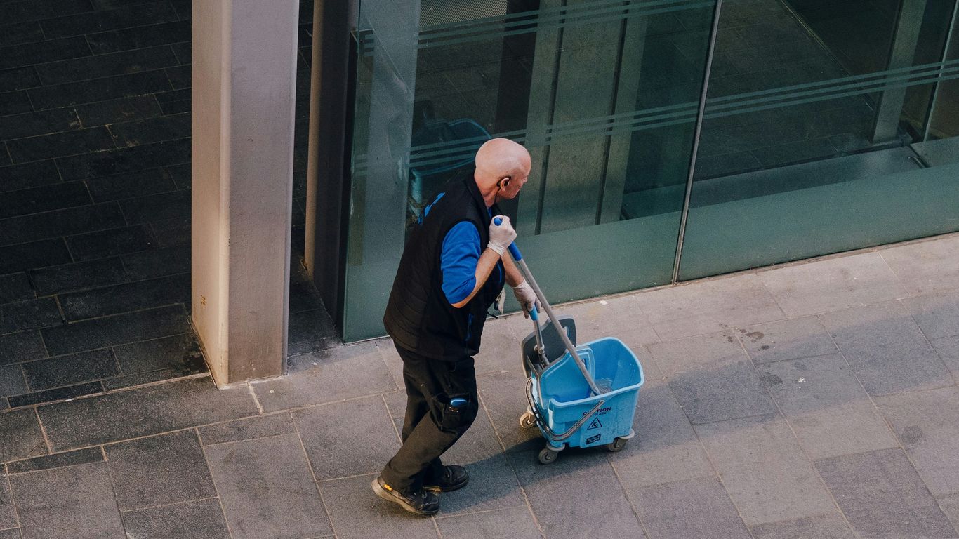 A man pulls a cleaning cart near a building.