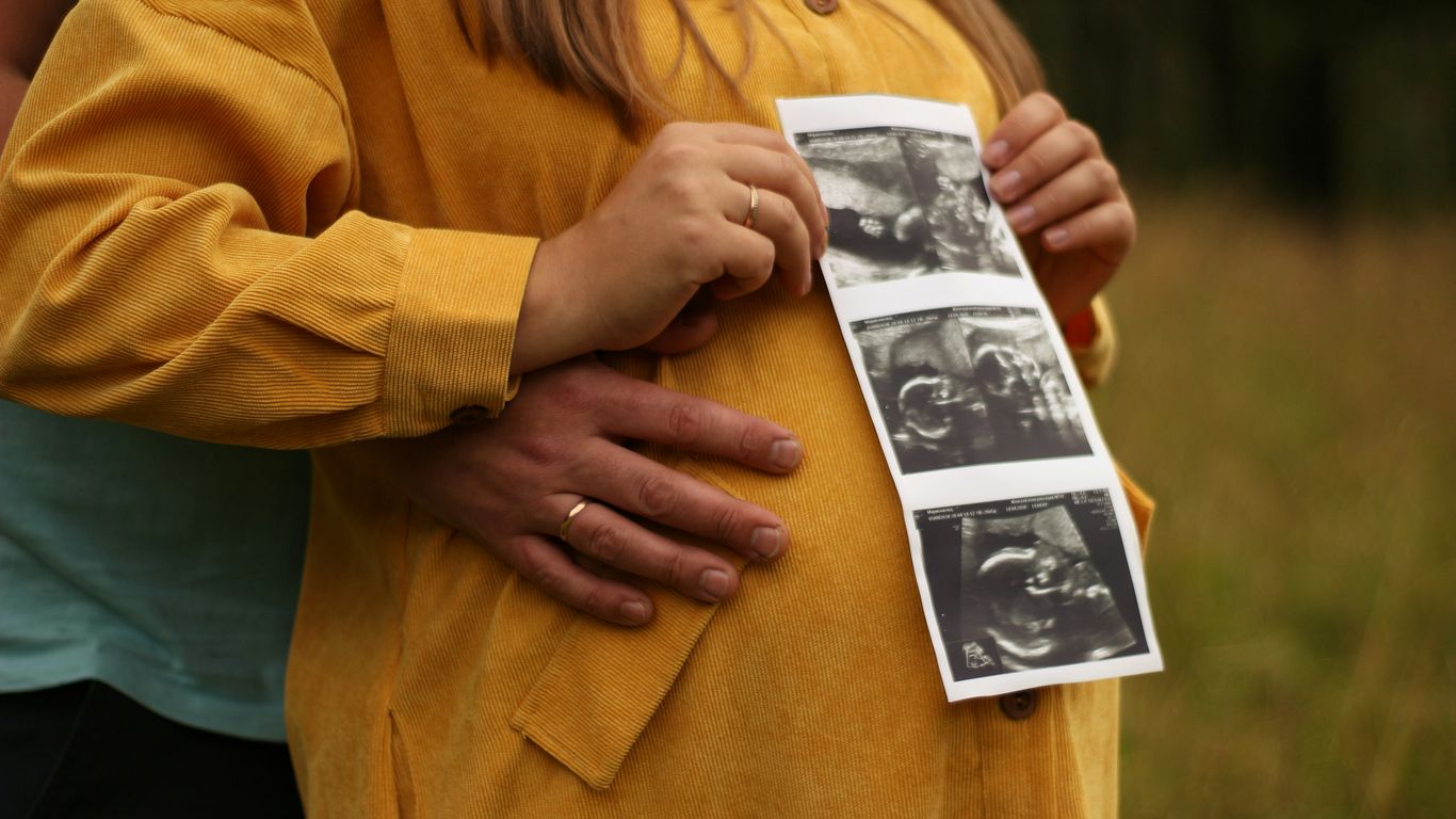 woman in brown coat holding picture of man in black shirt