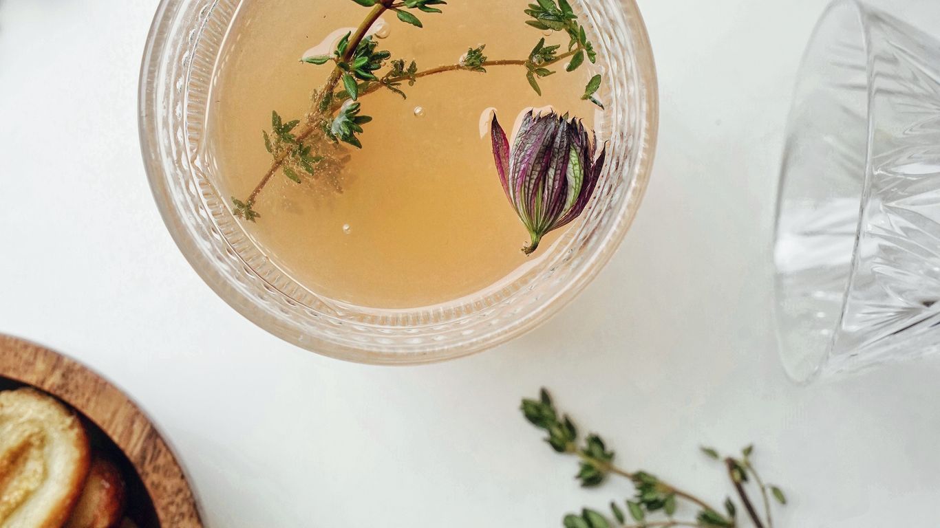 Herbal drink with flower garnish, cookies, and scattered fresh herbs.