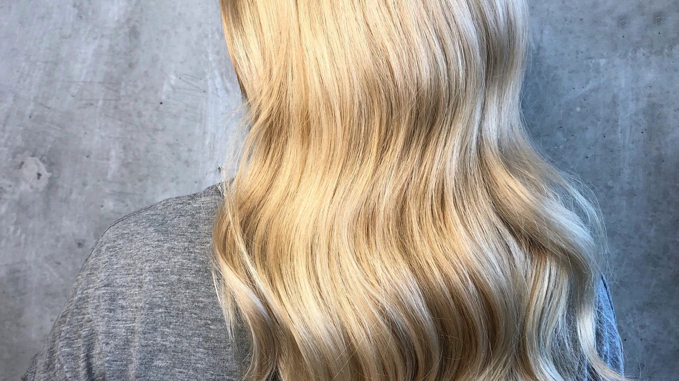 Blonde hair with soft waves against a grey background.