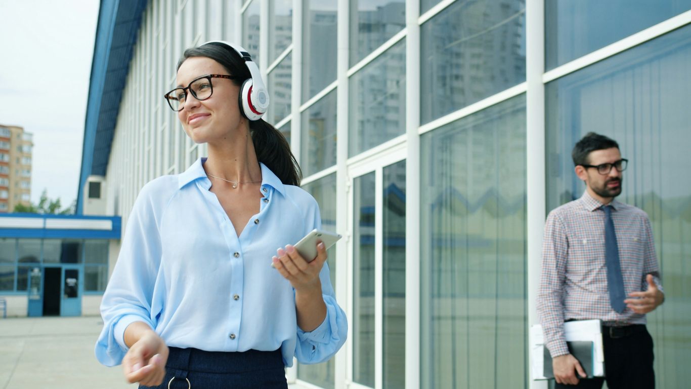 Woman with headphones walks past a man outside building