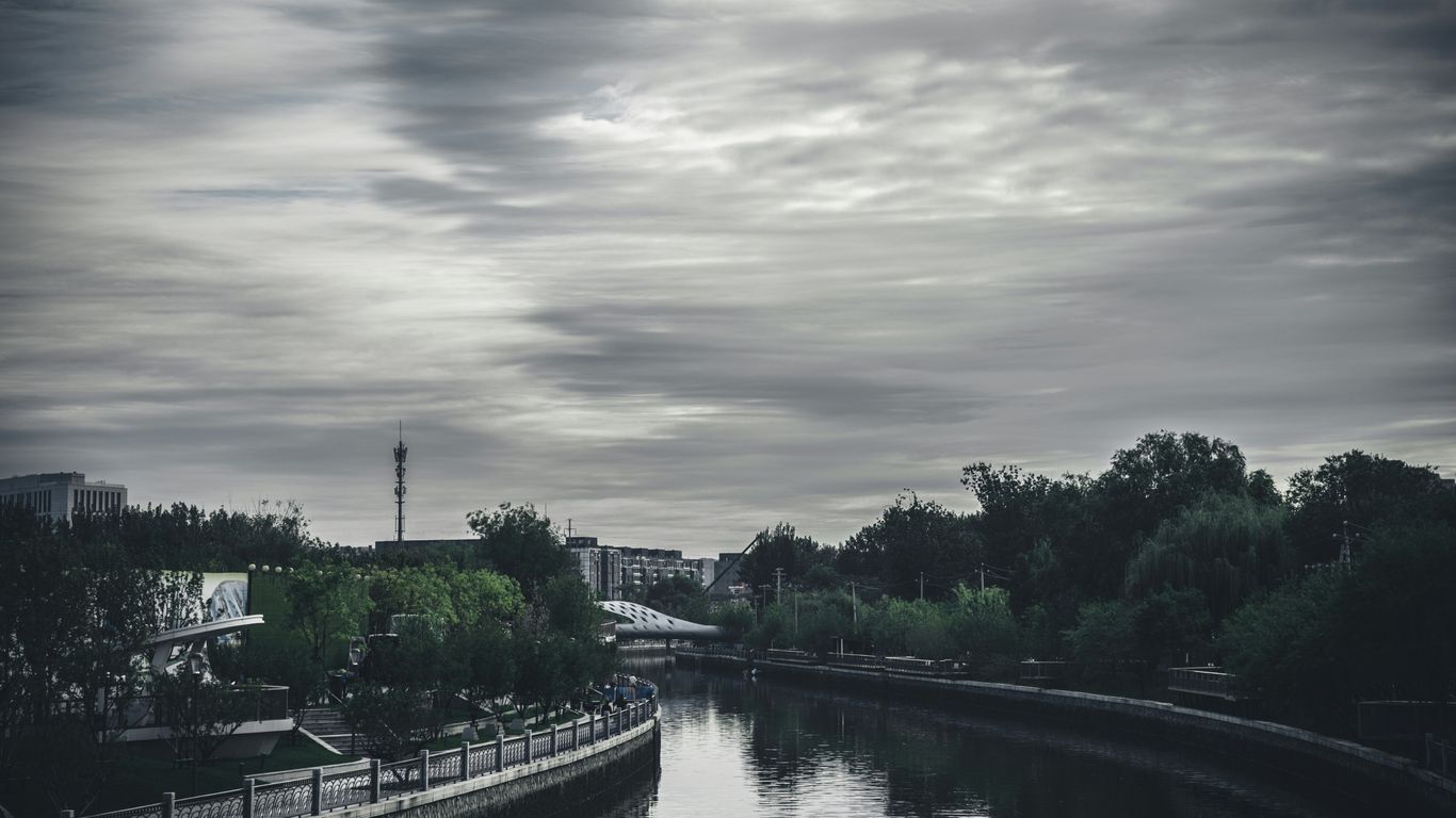 River flows through a city park under cloudy skies.