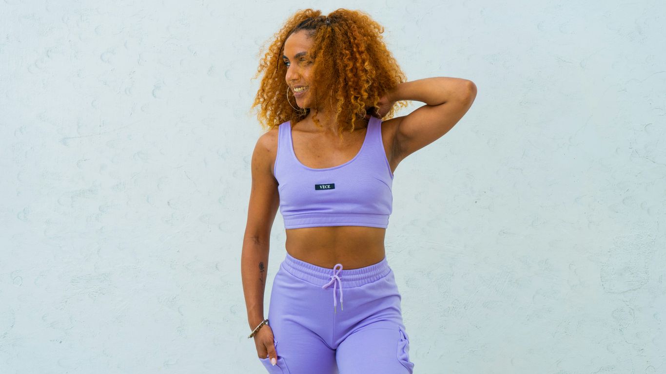 a woman with curly hair wearing a purple sports bra top and matching leggings