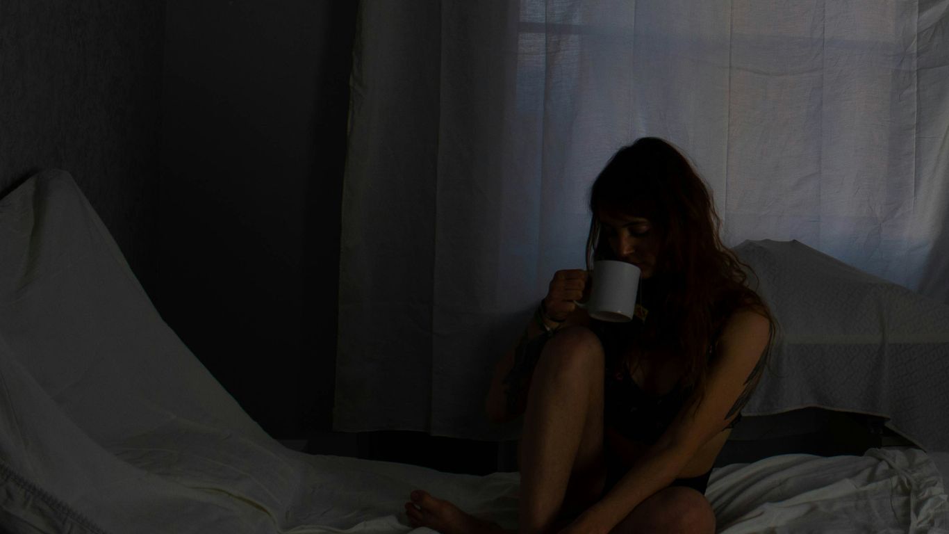 a woman sitting on a bed drinking a cup of coffee