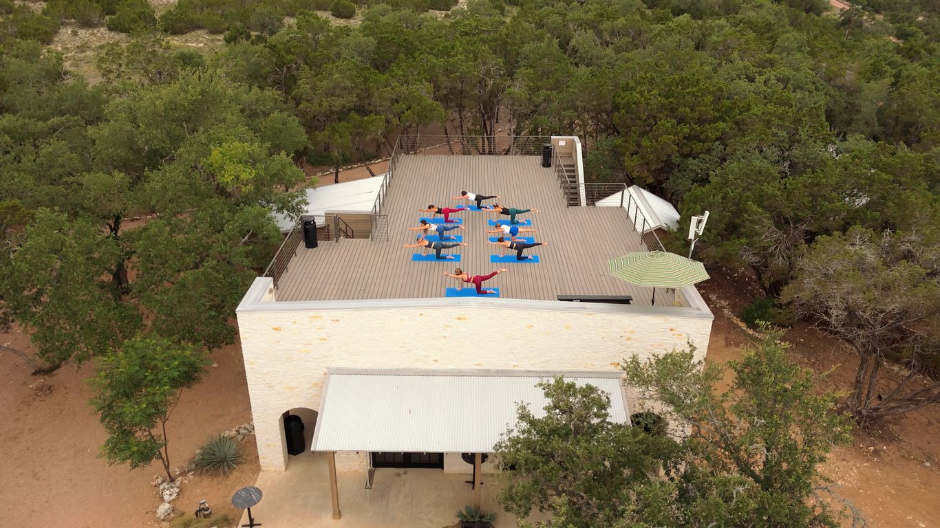 People practicing yoga on a rooftop surrounded by trees.